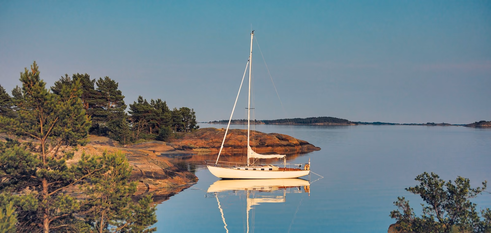A sailing yacht at anchor in a calm, pine-fringed bay on a mile-building cruise